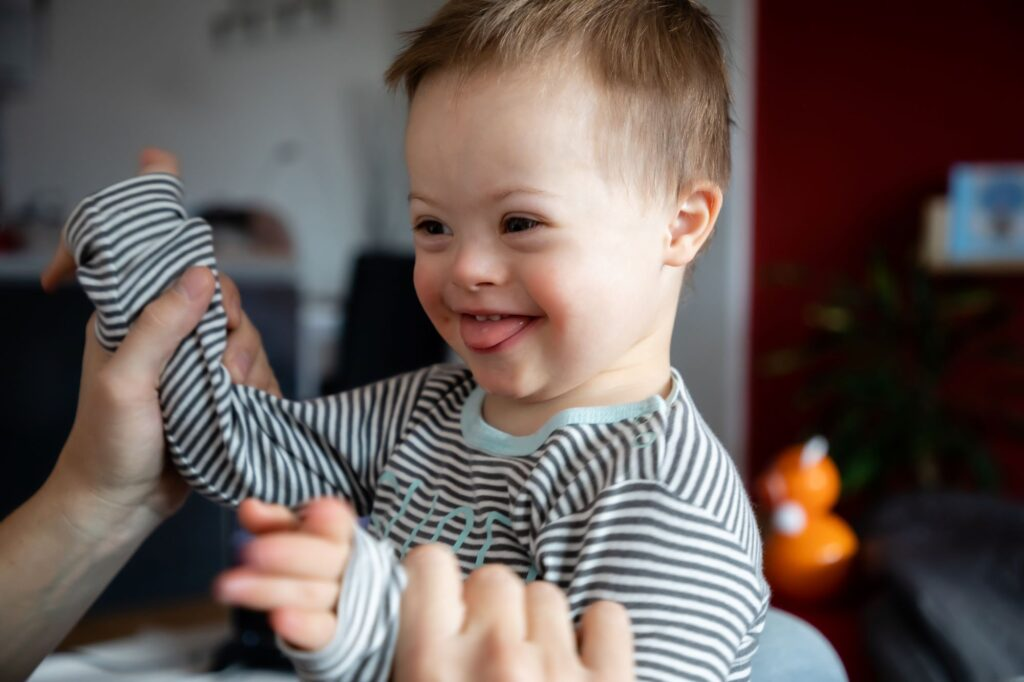 Joyful toddler with Down syndrome laughs while being supported by a parent at home — capturing the unconditional love of a mom of special needs, and celebrating early childhood development, neurodiversity, and emotional growth in children with disabilities.