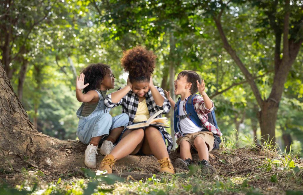 Autistic girl covers her ears while sitting under a tree, visibly overstimulated by outdoor sounds, as her mom of special needs and sibling try to support her — portraying sensory overload, emotional regulation, and real-life challenges faced by families raising children with autism.