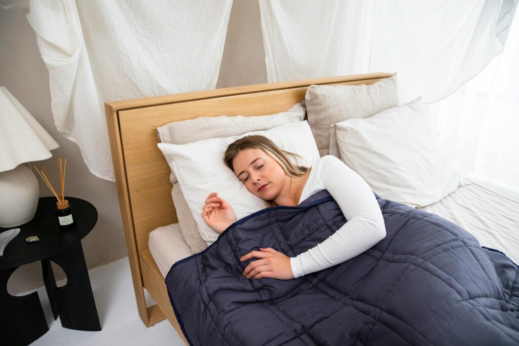 Adult woman resting peacefully in a calm, minimalist sensory-friendly bedroom with a weighted blanket, soft lighting, and calming decor — ideal for autistic adults