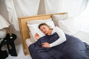 Adult woman resting peacefully in a calm, minimalist sensory-friendly bedroom with a weighted blanket, soft lighting, and calming decor — ideal for autistic adults