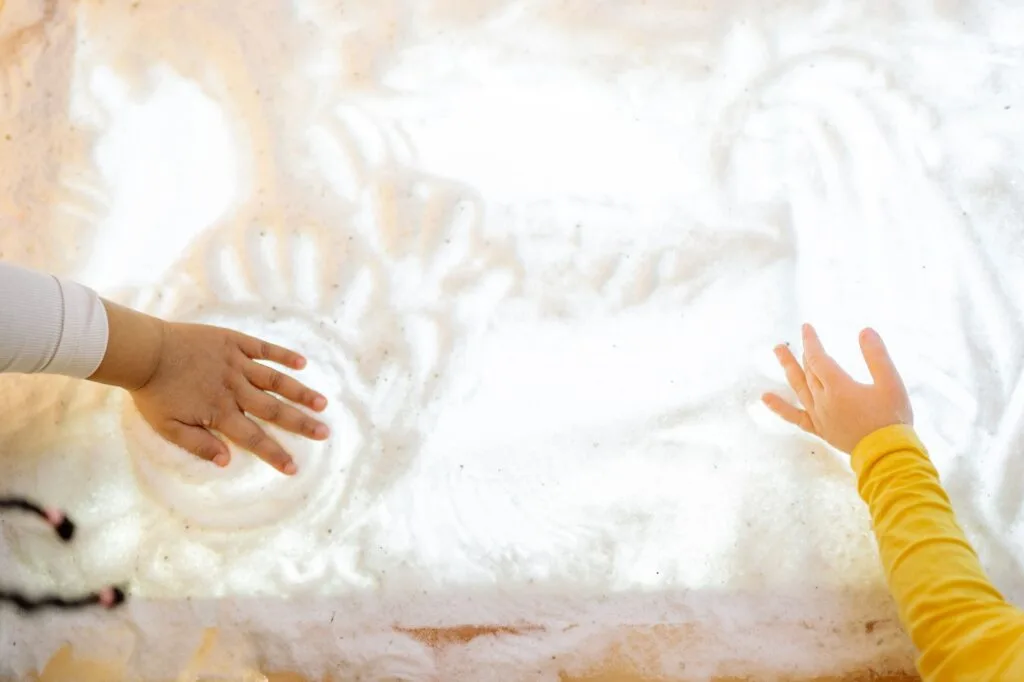 Two children exploring a sensory light table with their hands, showing tactile and visual stimulation with sensory toys for autism and sensory processing disorder