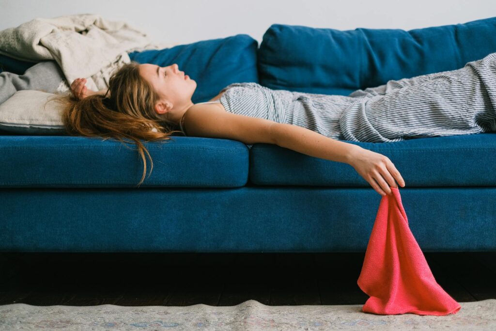 Exhausted woman lying flat on a blue couch, arms limp and head back, depicting the real physical and emotional fatigue of special needs mom burnout