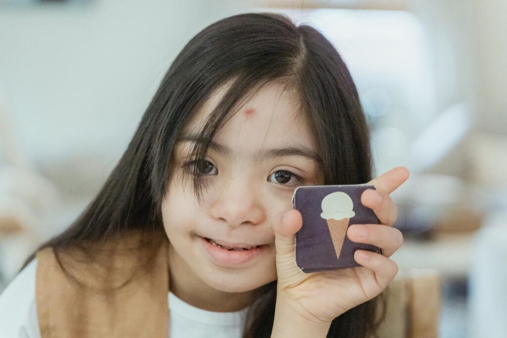 Young girl with Down syndrome smiling and holding a memory game card, representing the rising autism and developmental disability rates in 2026