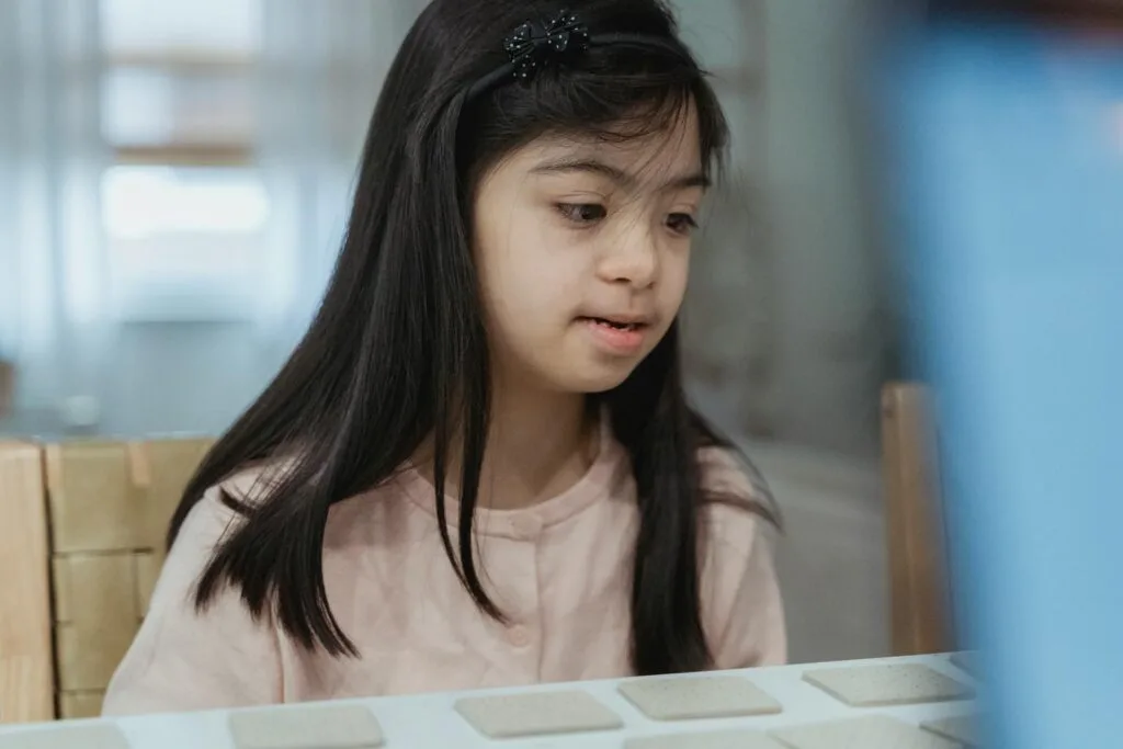 Girl with Down syndrome focused and calm while playing at a table, representing the peace and organization of a sensory-friendly bedroom for a child with autism
