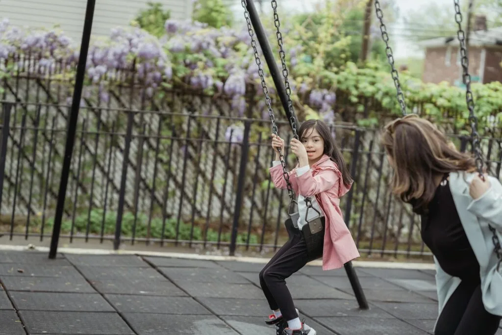 Girl with Down syndrome enjoying a sensory swing at a playground, showing vestibular input and movement therapy for autism