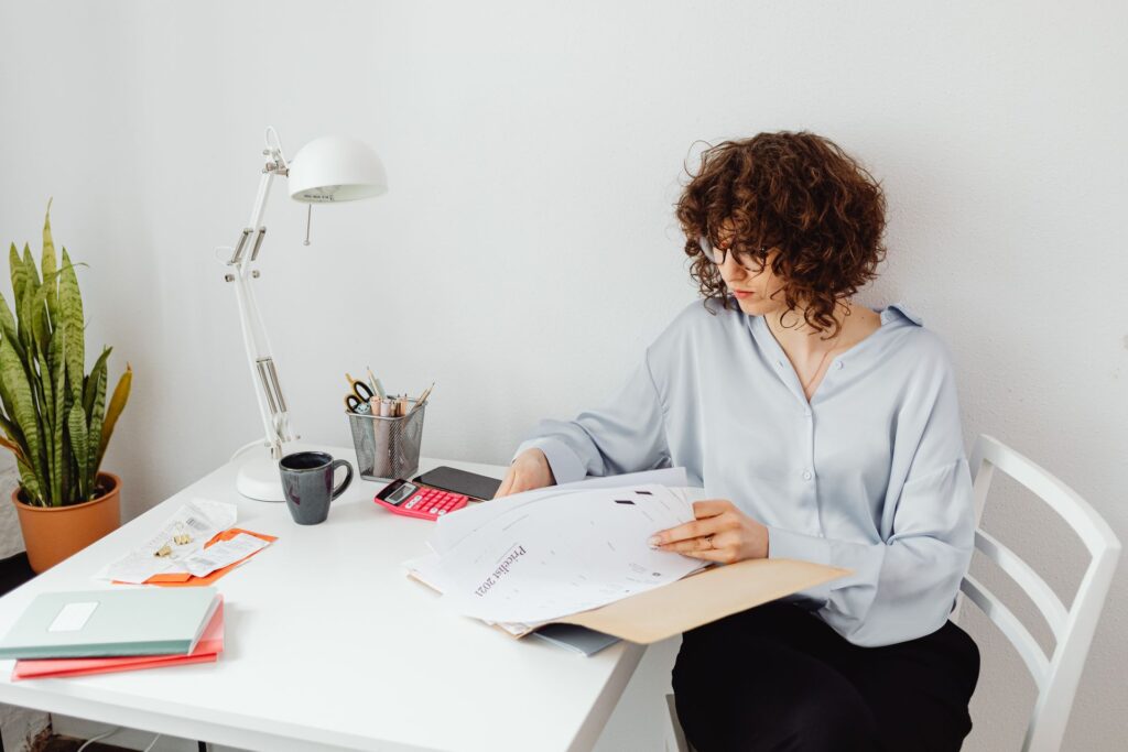 Woman carefully reviewing paperwork and documents at a home office desk with a coffee mug, representing a special needs mom preparing to advocate at an IEP meeting