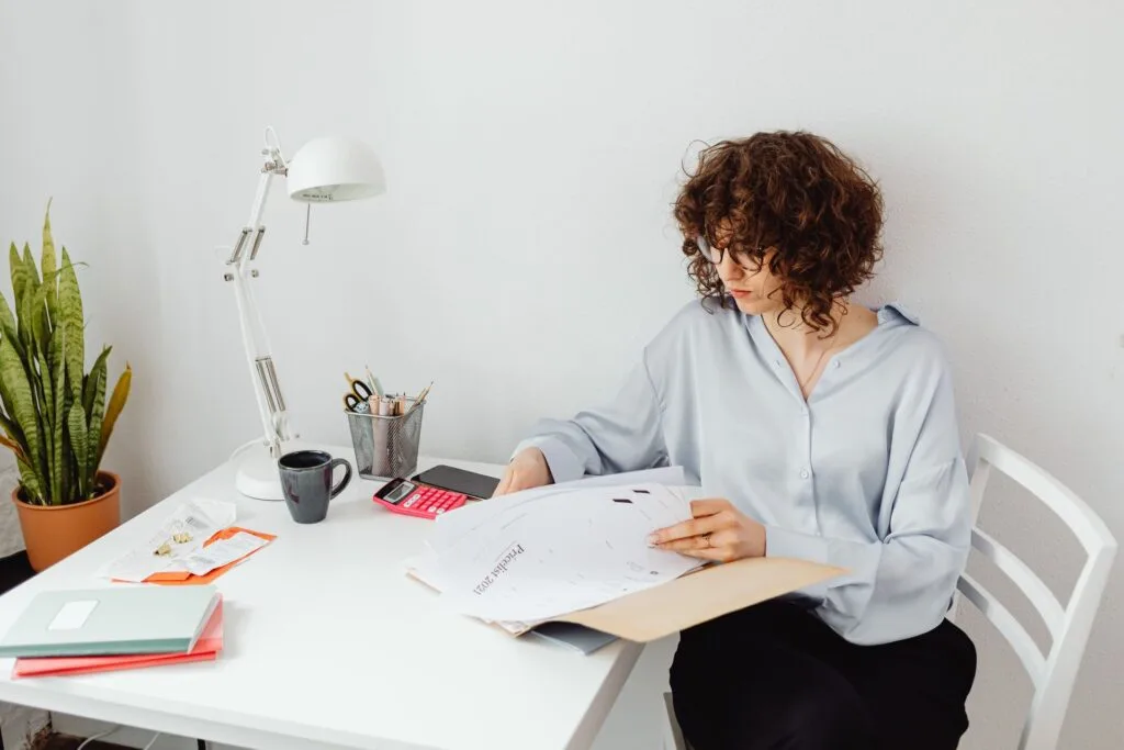 Woman carefully reviewing paperwork and documents at a home office desk with a coffee mug, representing a special needs mom preparing to advocate at an IEP meeting