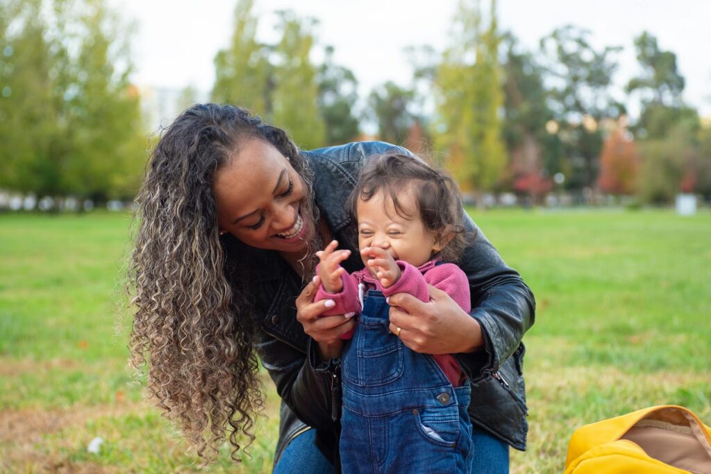 Loving mother holding her baby with Down syndrome outdoors in a park, capturing the tender bond after an autism or disability diagnosis
