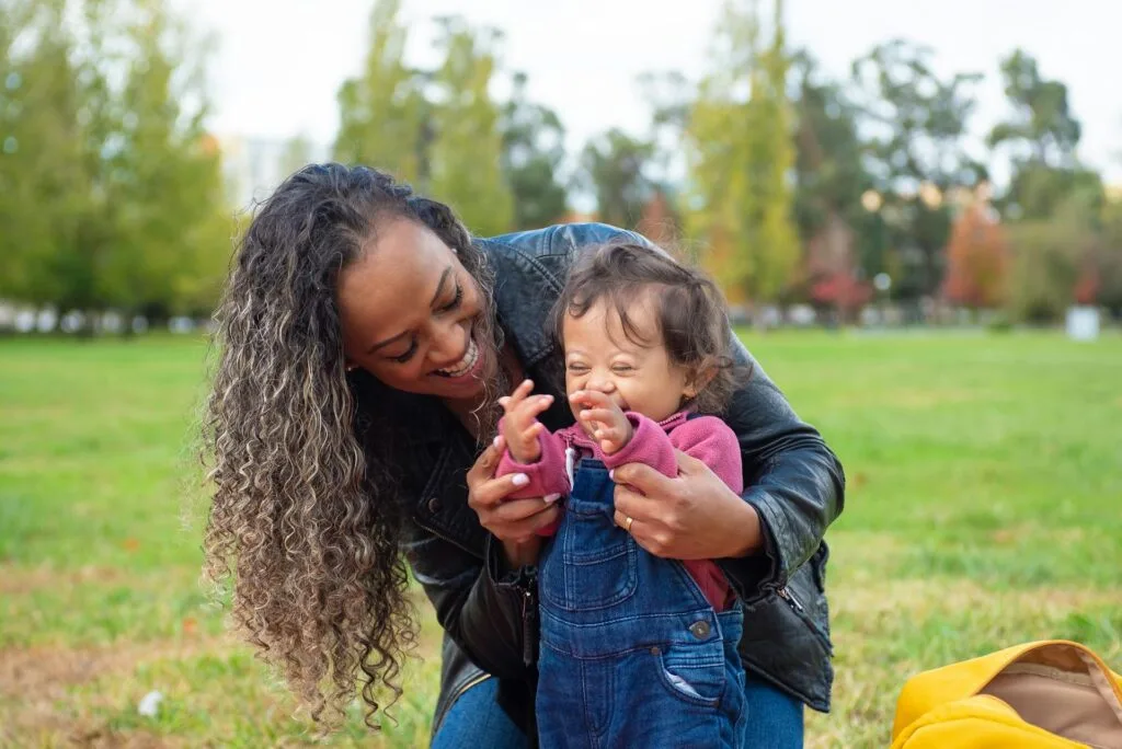 Loving mother holding her baby with Down syndrome outdoors in a park, capturing the tender bond after an autism or disability diagnosis