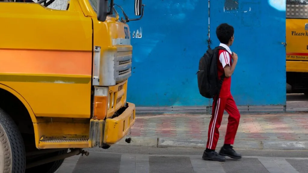 Autistic child with backpack standing at bus stop facing an autism school transition