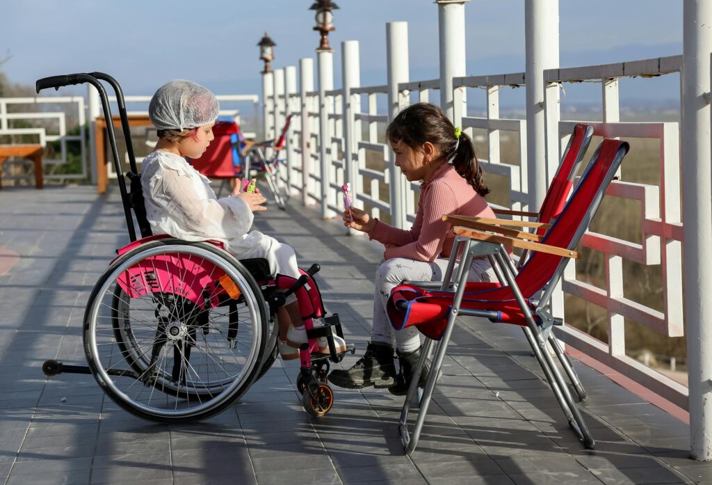 Two young girls together - one in a wheelchair with AFO braces and one sitting beside her, representing the sibling relationship when raising a child with special needs