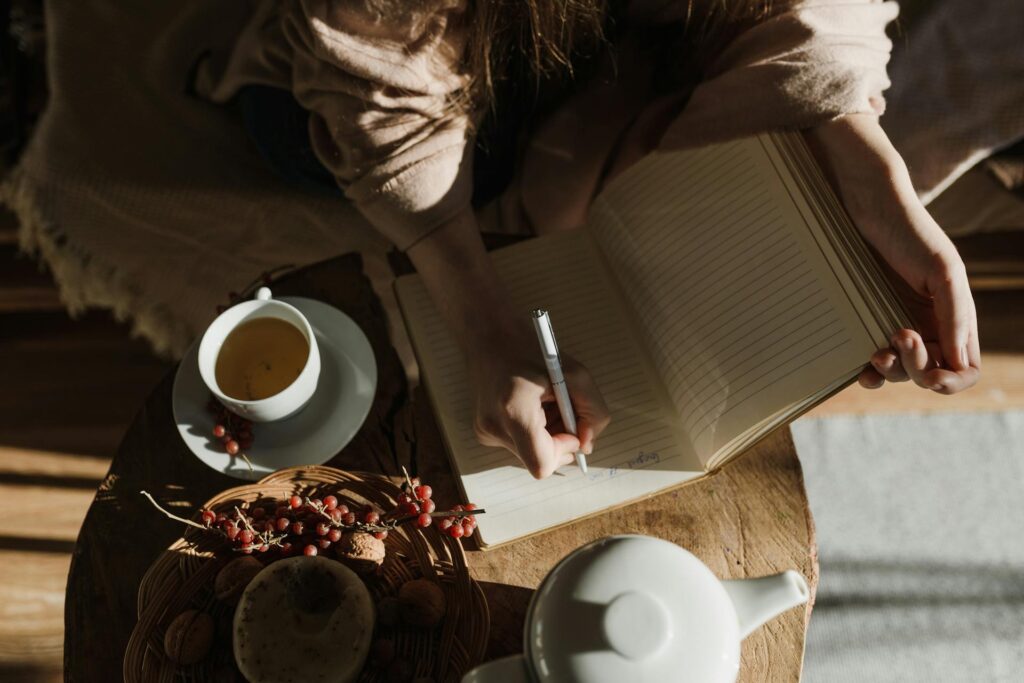 Woman writing in a journal beside a cup of tea in warm natural light, representing a quiet self-care moment for special needs moms
